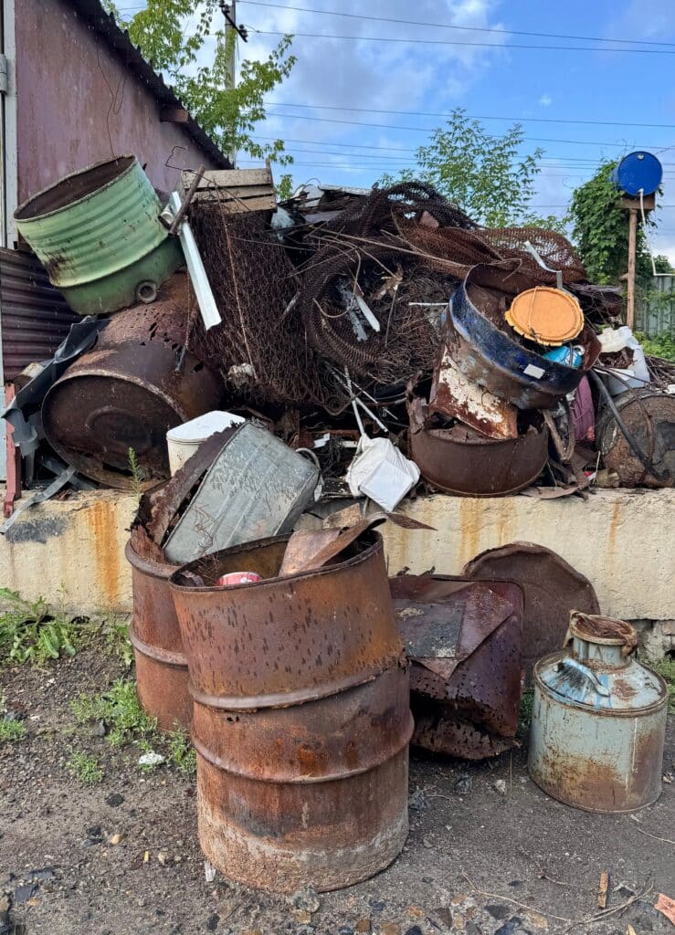 Ferraille rouillée : fûts, tôles et déchets métalliques Grosses accumulations de fûts rouillés, fers à béton et débris métalliques sur un tas de ferraille sous un ciel nuageux.