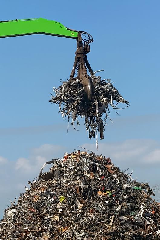 Ferraille métallique traitée par une grue : recyclage industriel Grue chargeant de la ferraille métallique hachée sur un tas énorme sous un ciel bleu clair.