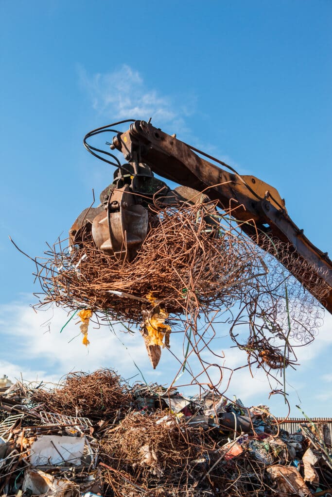 Recyclage de ferraille : Grue soulevant des déchets métalliques Grue à pince ramassant une grosse touffe de ferraille rouillée et de grillages, ciel bleu.